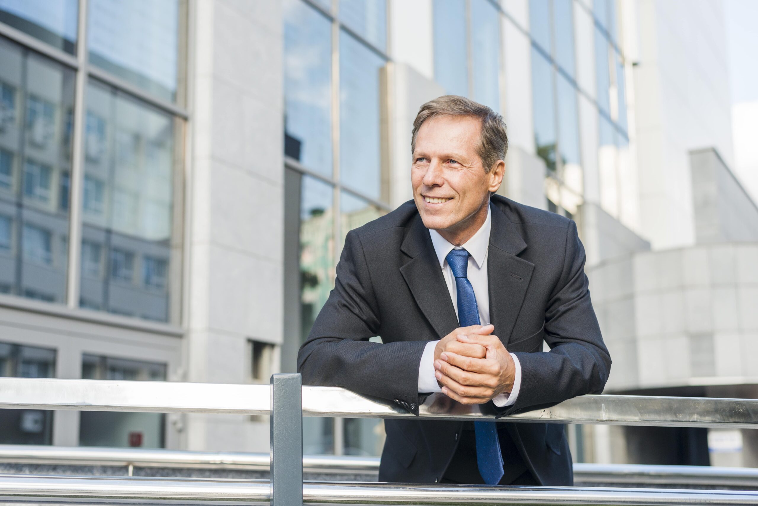 portrait smiling mature businessman leaning railing min scaled